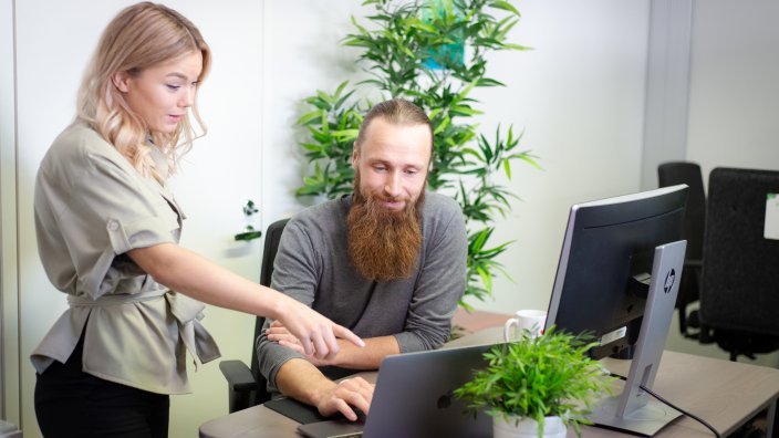 Henkilö osoittaa tietokoneen näytöllä näkyvää toiselle henkilölle