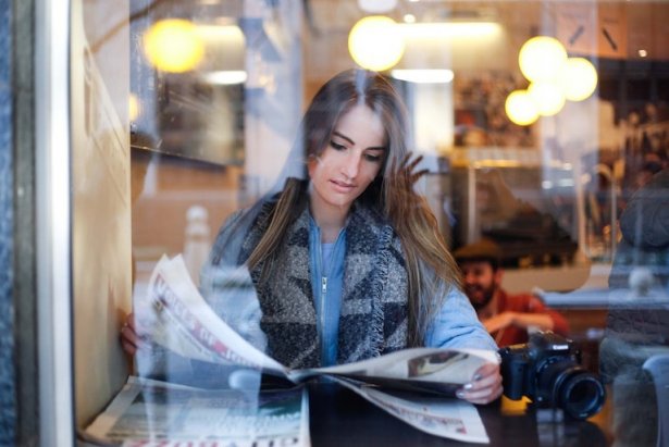 Nainen lukee sanomalehteä ravintolassa
