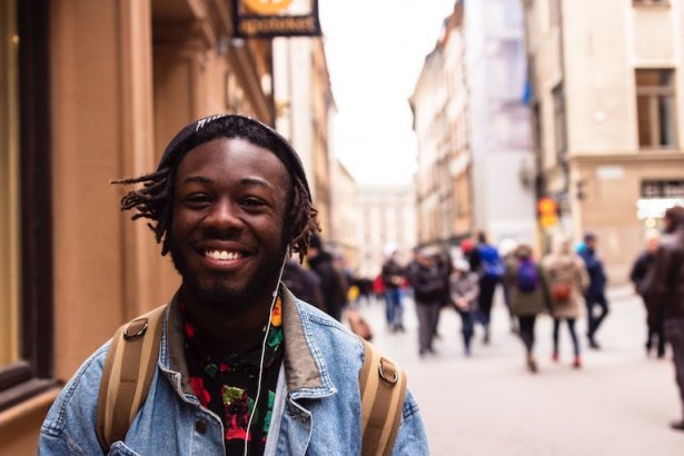 Hymyilevä kansainvälinen opiskelija kävelee kadulla ja kuuntelee musiikkia